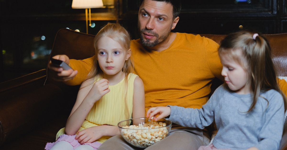 Père et ses deux filles assis sur le canapé partageant du popcorn pendant une soirée cinéma à la maison